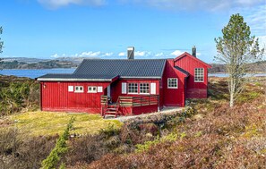 A red wooden house with a black roof, a chimney, and a small porch.