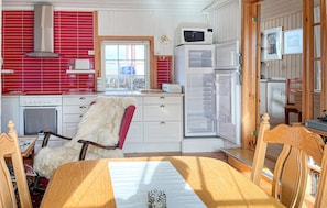 A kitchen with a red tiled backsplash, white cabinetry, a wooden dining table, and a refrigerator.