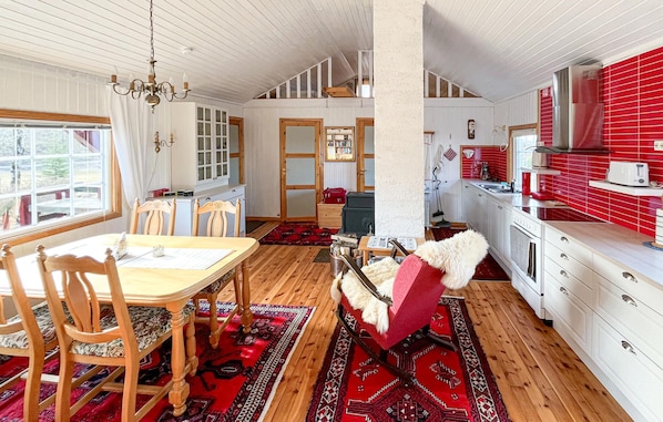 A cozy kitchen with a dining area, wooden floors, and a red and white color scheme.