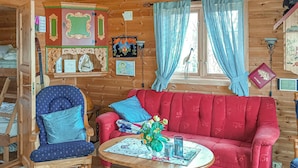Une pièce chaleureuse avec un canapé rouge, une chaise en bois, une petite table sur laquelle est posé un vase de fleurs, et divers tableaux encadrés accrochés aux murs.