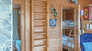 L’intérieur d’un chalet en bois, avec un lit superposé, une échelle, une petite étagère ornée d’objets décoratifs et un mur en pierre.