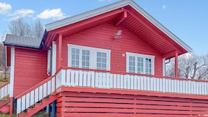 Une maison en bois rouge avec des ornements blancs, un porche et un escalier menant à l’entrée.