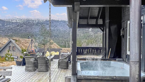 Eine Holzterrasse mit Sitzgelegenheiten im Freien, einem Whirlpool und Blick auf schneebedeckte Berge.