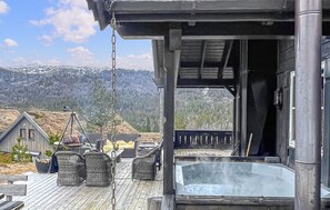 A wooden deck with outdoor seating, a hot tub, and a view of snow-capped mountains.