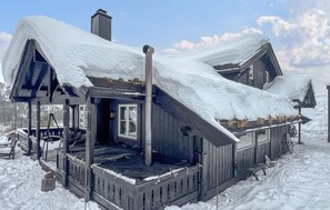 A wooden cabin with a steeply pitched roof, surrounded by snow.
