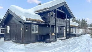 Ein dunkles Holzhaus mit verschneietem Dach und einem Balkon.