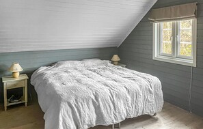 A bedroom with a sloped ceiling, a bed with a white bedspread, a nightstand with a lamp, and a window with a view of trees. - Amazing home in Lindesnes with WiFi (Lindesnes)