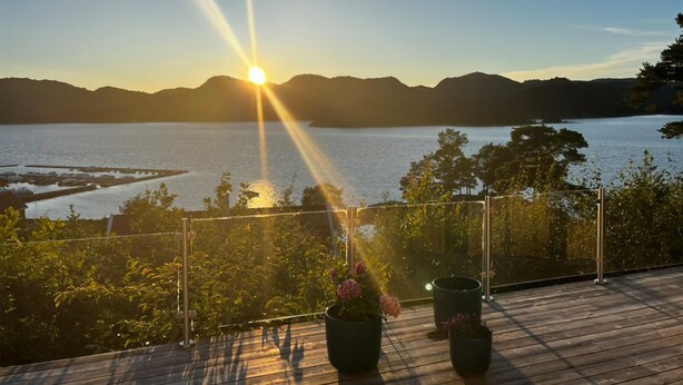 Ett trädäck med krukväxter, med utsikt över en sjö eller ett annat vattendrag och avlägsna berg under solnedgången.