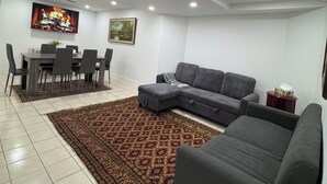 A living room with a dining area, a gray sofa, a patterned rug, and a painting on the wall.