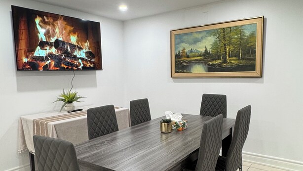 A dining area with a long table, six chairs, a rug, and two paintings on the walls.