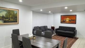 Un salon moderne avec une table à manger, des canapés gris recouverts de tissu et deux tableaux accrochés aux murs.