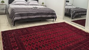 A bedroom with a bed, a mirror, a red rug, and a nightstand with a plant.