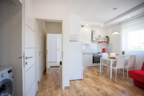 A modern kitchen with white cabinetry, a dining area with a table and chairs, and a red sofa. - Sun And Fun, Pula, Croatia (Pula)