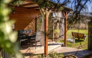 Una cabana de fusta amb un espai de terrassa que compta amb una taula, cadires i una cadira espanyola.