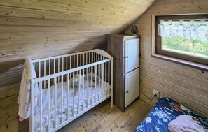 Habitació de cabana de fusta amb bressol, un petit armari i finestra amb vistes.