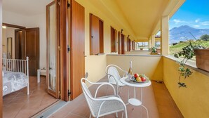 A balcony with a table set for two, a bed, and a view of a mountain. - Residence La Perla - Apt 36, Monte Isola, Italy (Monte Isola)
