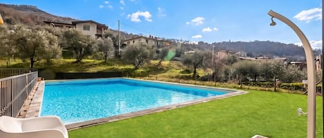 A swimming pool with a clear blue water surface, surrounded by a well-maintained lawn and a few trees.
