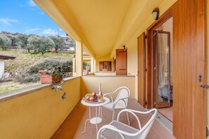 A balcony with two white wicker chairs, a small round table, and a fruit and bottle arrangement. - Residence La Perla - Apt 39, Monte Isola, Italy (Monte Isola)