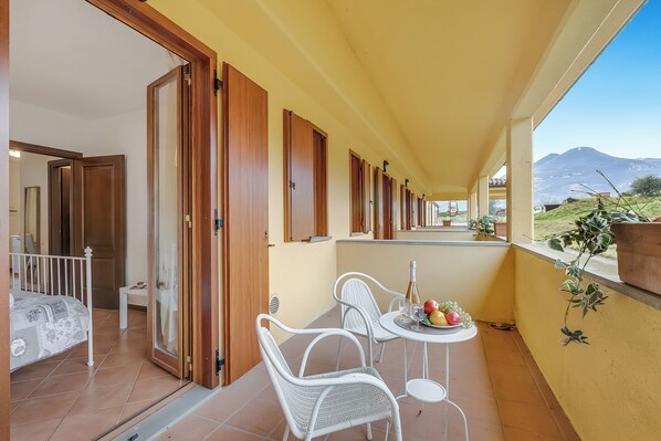 A balcony with a table set for two, a bed, and a view of a mountain. - Residence La Perla - Apt 35, Monte Isola, Italy (Monte Isola)