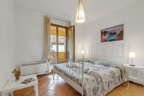 A bedroom with a bed, bedside lamps, a window with curtains, a painting on the wall, and a small table with a vase and magazine. - Residence La Perla - Apt 35, Monte Isola, Italy (Monte Isola)