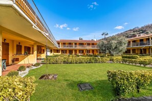 A courtyard with a lawn, hedges, and a building with balconies. - Residence La Perla - Apt 35, Monte Isola, Italy (Monte Isola)