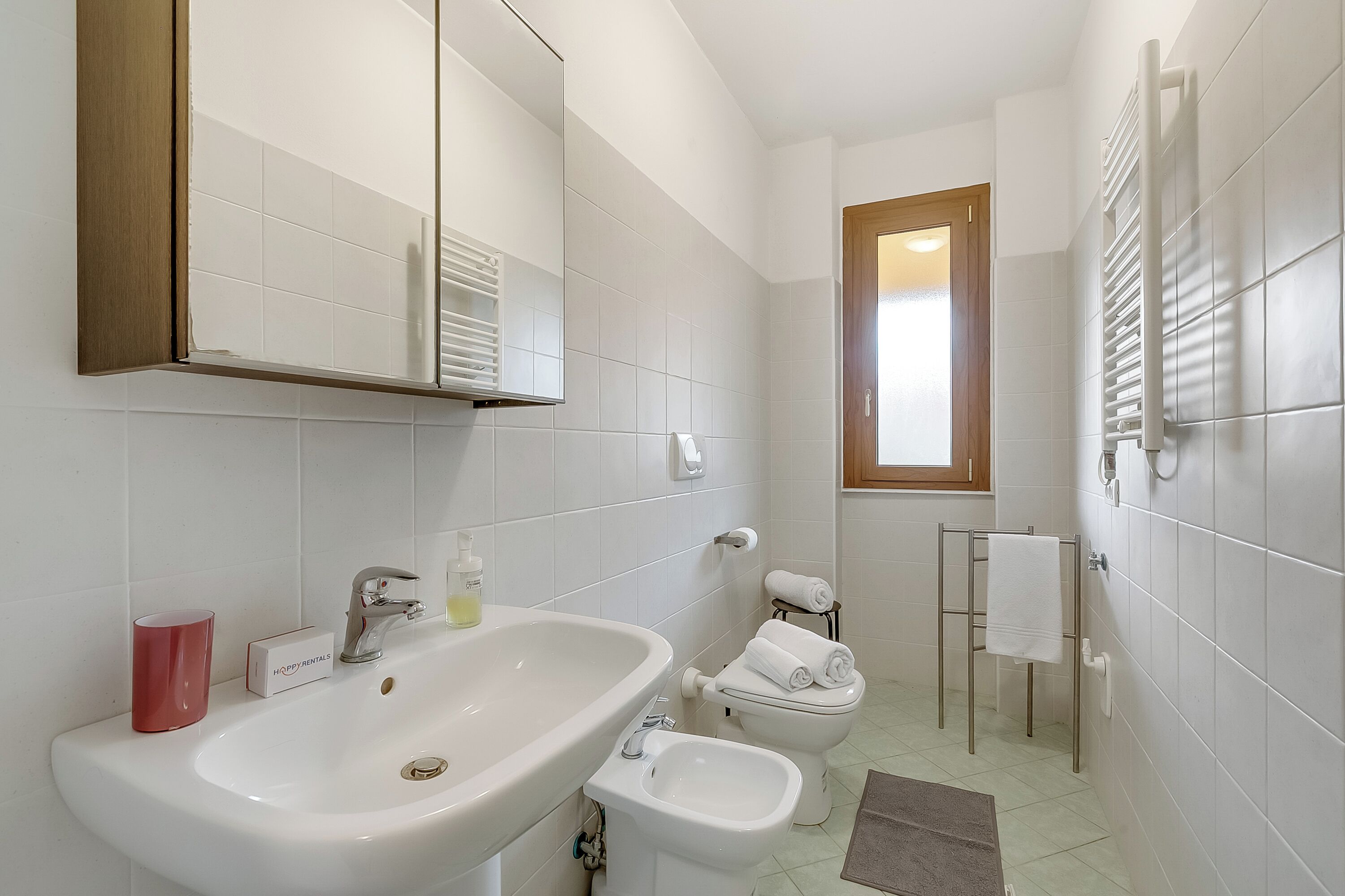 A bathroom with a sink, bidet, toilet, towel rack, and a mirror.