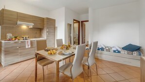A modern kitchen with a dining area, featuring a white table, two chairs, and a sofa with a blue pillow. - Residence La Perla - Apt 41, Monte Isola, Italy (Monte Isola)