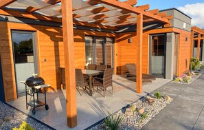 Ein modernes Holzhaus mit überdachter Terrasse, Gartenmöbeln und Grill.