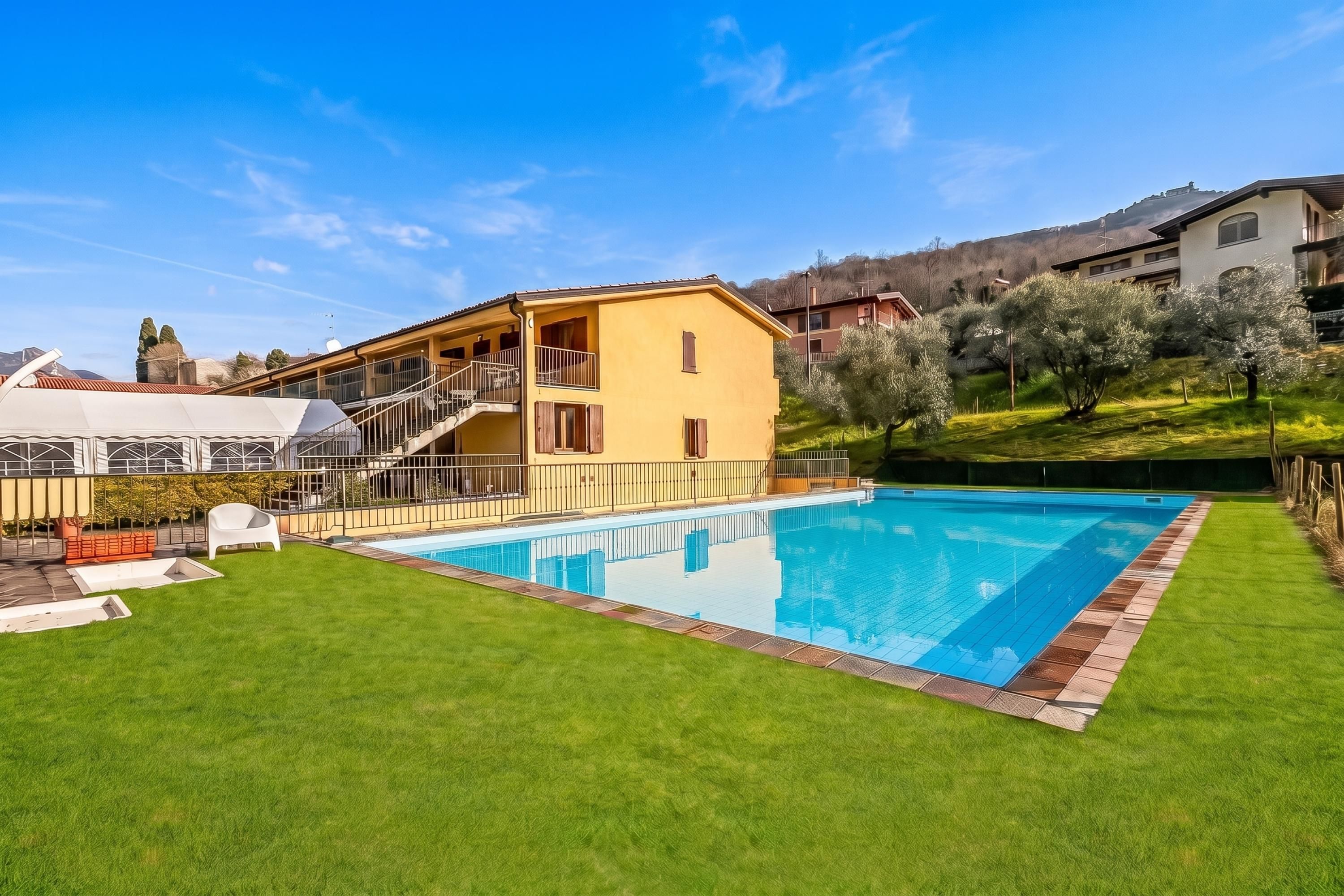 A residential property with a swimming pool, a well-maintained lawn, and a two-story house with a balcony.