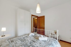 A bedroom with a bed, a bedside table with a lamp, a wardrobe, and a door leading to another room. - Residence La Perla - Apt 33, Monte Isola, Italy (Monte Isola)