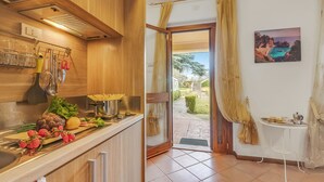 A kitchen with wooden cabinets, a countertop with fresh produce, and a view of the outdoors through a glass door. - Residence La Perla - Apt 09, Monte Isola, Italy (Monte Isola)