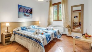 A bedroom with a bed, nightstands, a window with curtains, a painting, and a table with a bottle and fruit. - Residence La Perla - Apt 09, Monte Isola, Italy (Monte Isola)