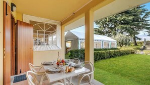 Un espacio de comedor al aire libre con una mesa dispuesta para dos personas, una puerta de madera y vistas al jardín y otros edificios.