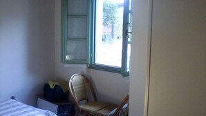 A bedroom with a bed, a chair, a window, and a small table with a bag. - Cibo 17 - Two-room apartment with sea view (Capraia Isola)
