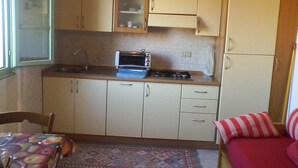 A compact kitchen with a microwave, cabinets, and a dining area with a table and chairs. - Cibo 17 - Two-room apartment with sea view (Capraia Isola)