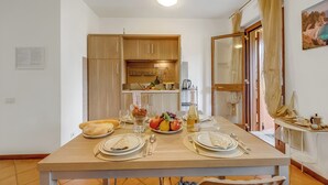 Comedor con una mesa dispuesta para cuatro, cocina al fondo y vista a través de un ventanal.