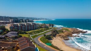 Un hotel frente al mar con varias construcciones, una playa y un litoral rocoso.