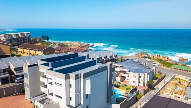 Una zona residencial costera con edificios modernos, vista al océano y cielo despejado.