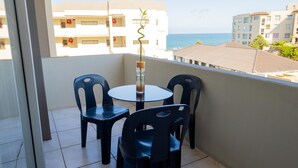 Un balcón con mesa y sillas, con vista al mar y edificios costeros.