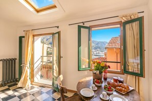A room with a checkered floor, a table set for breakfast, a view of a mountain, and a balcony with a view. - House Old Town 50m Beach and Shop, Menton, France (Menton)