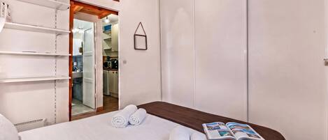 A hotel room with a bed, a wardrobe, a shelf unit, and a door leading to a bathroom.
