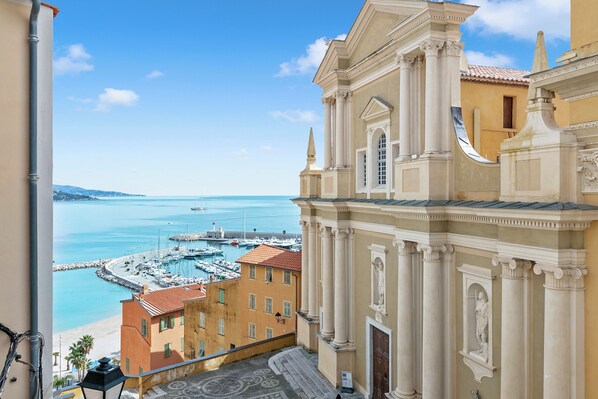 Un edificio costero de arquitectura clásica, con vistas al mar y un puerto deportivo con barcos.