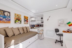 A modern living room with a sofa, a dining area with a chair, a kitchen with a sink, and a clock on the wall. - Studio Old Town 50m Beach and Shop, Menton, France (Menton)