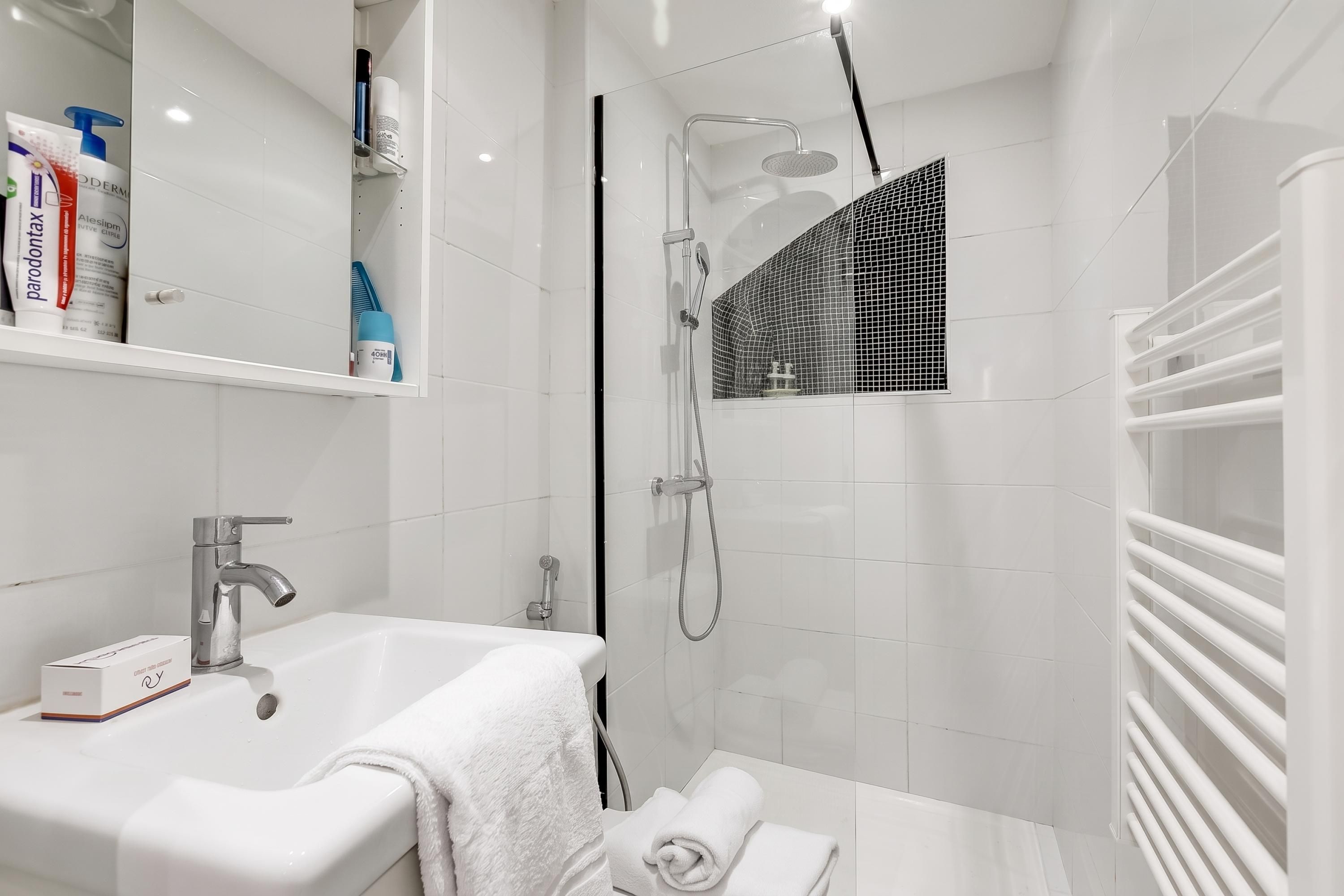 Une salle de bain moderne avec un lavabo blanc, une douchette à main et une douche à parois de verre.
