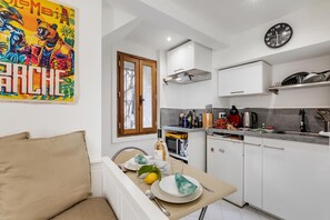 A modern kitchen with a dining area, a clock, and a colorful artwork on the wall. - Studio Old Town 50m Beach and Shop, Menton, France (Menton)