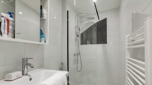 Un baño moderno con lavamanos, espejo, ducha y toallero.