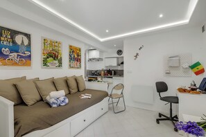 Ein modernes Zimmer mit Sofa, Schreibtisch, Stuhl, Küchenzeile und Bildern an den Wänden.
