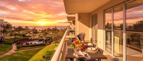A balcony with a table set for dining, overlooking a pool and lush greenery.