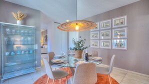 Un coin repas avec une table en verre, des chaises grises, un luminaire suspendu en osier et des tableaux encadrés au mur.