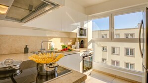 Une cuisine moderne équipée d’une cuisinière, d’un évier et d’une fenêtre donnant sur un immeuble.